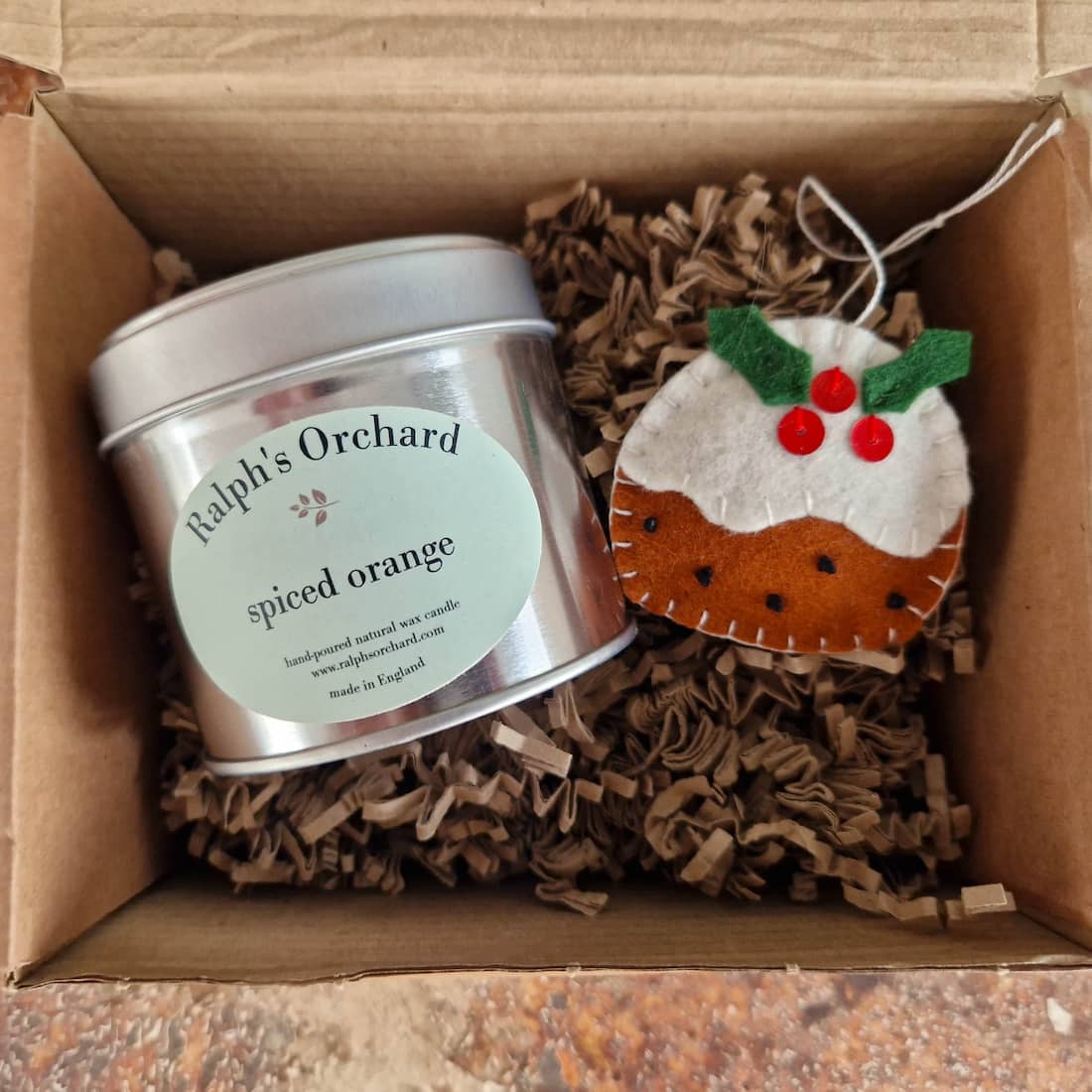 Candle tin labeled 'Ralph's Orchard' and a Christmas-themed ornament in a box.