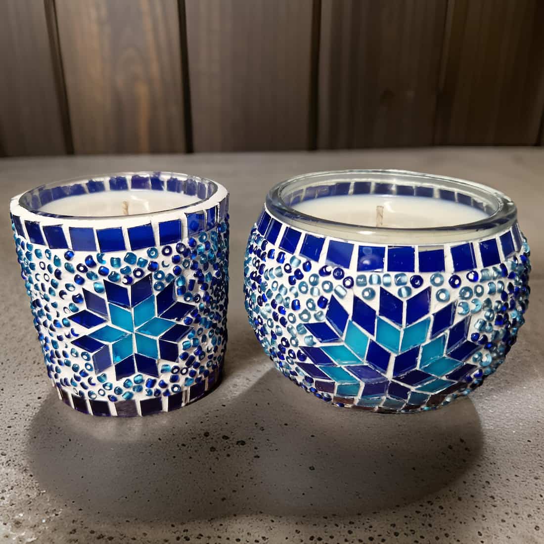 Two mosaic candle holders with blue and white patterns on a gray surface.