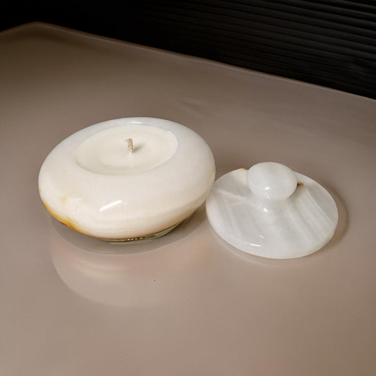White ceramic candle holder with a lid on a reflective surface