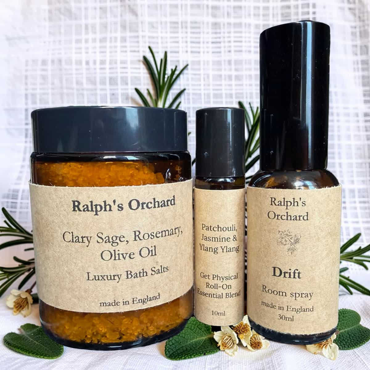 Three Ralph's Orchard products including bath salts, essential oil roll-on, and room spray on a white background with greenery.