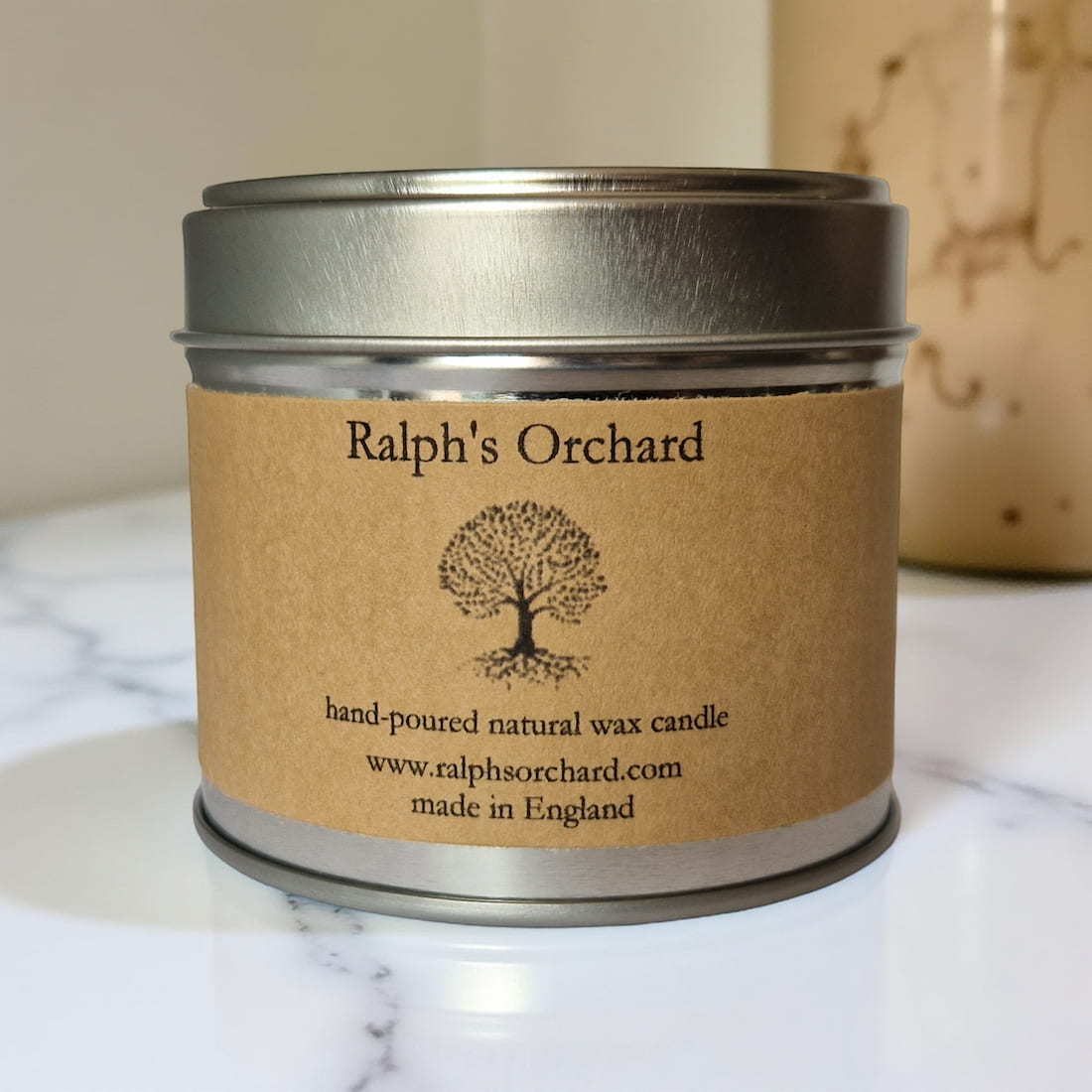 Candle in a tin labeled 'Ralph's Orchard' on a marble surface