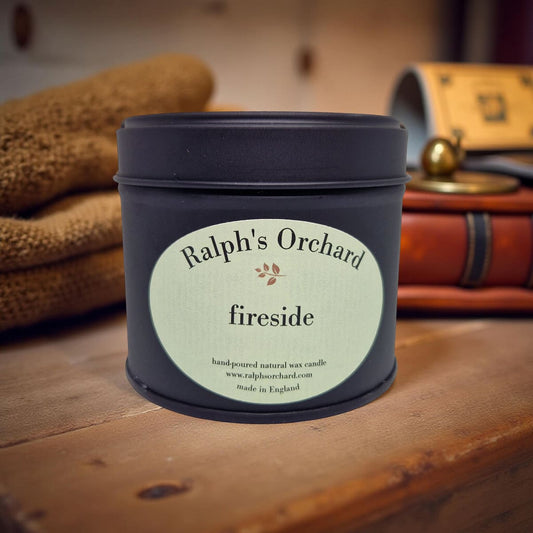 Candle jar labeled 'Ralph's Orchard fireside' on a wooden surface with a blurred background.