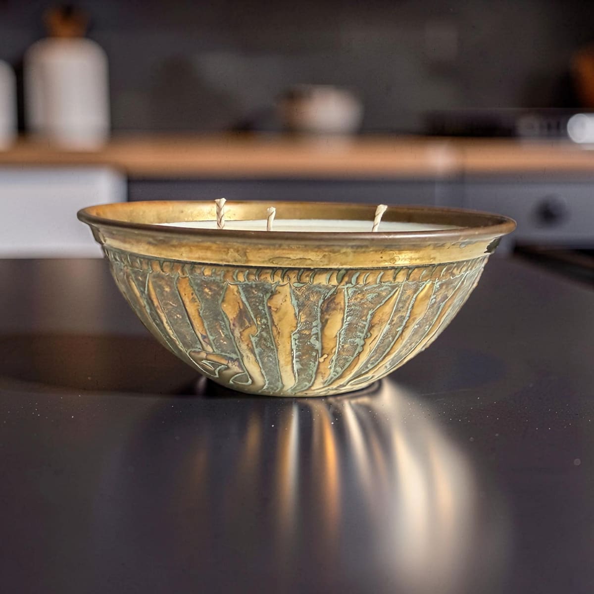 Decorative candle in a textured metal bowl on a reflective surface