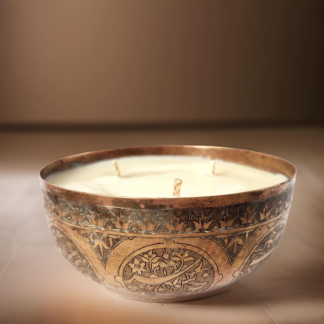 Decorative candle in an ornate bronze holder on a brown background