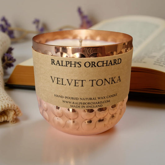 Candle with 'Ralph's Orchard Velvet Tonka' label in a textured container on a light surface.