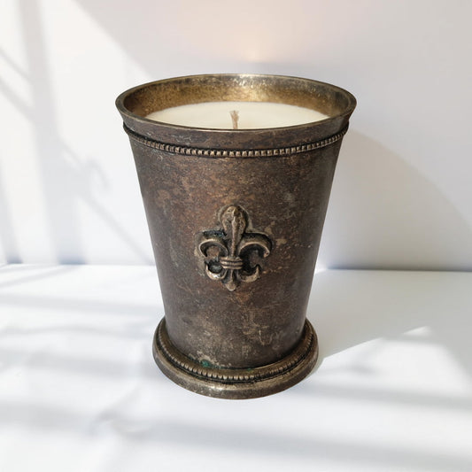 Decorative candle in a metal holder with a fleur-de-lis design on a white background