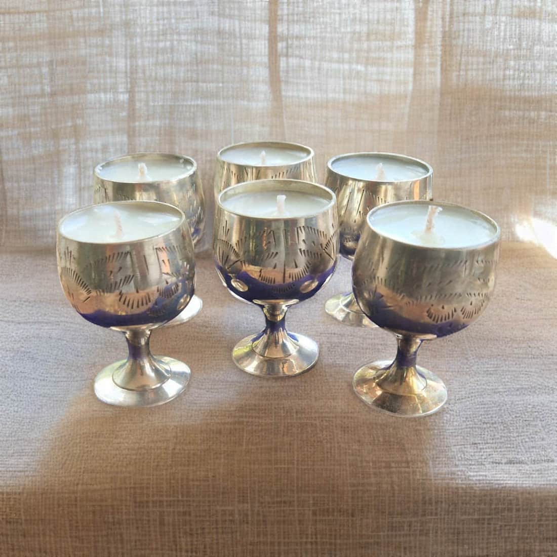 Set of six silver candle holders with candles on a textured surface