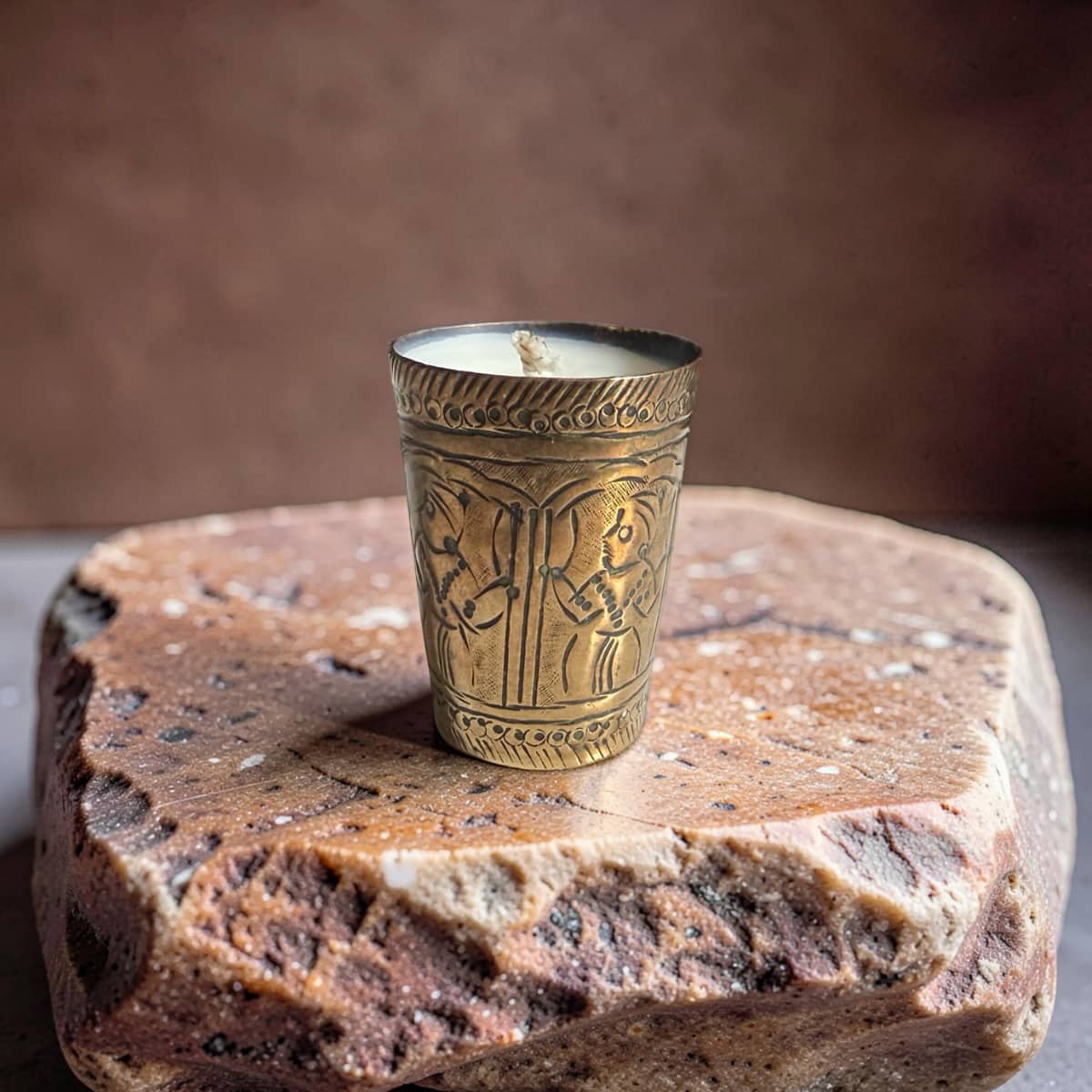 Decorative candle in an ornate brass holder on a stone surface with a brown background