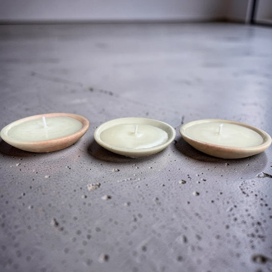 Three small round ceramic candle holders with lit white candles, arranged in a row on a textured gray concrete surface.