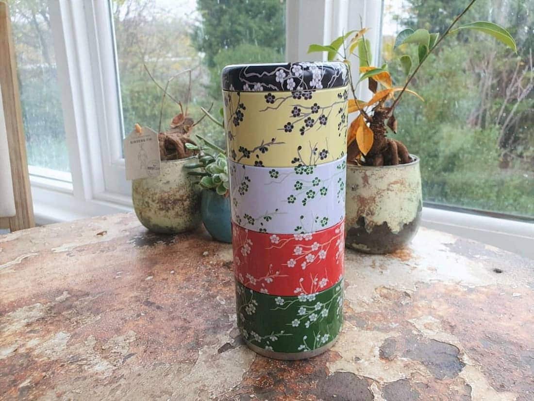 Colorful cylindrical container with floral patterns on a wooden surface with plants in the background