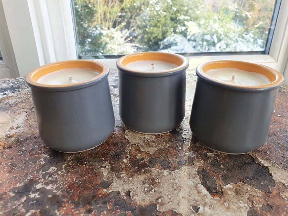 Three gray candle holders with orange rims on a stone surface, with a window in the background.