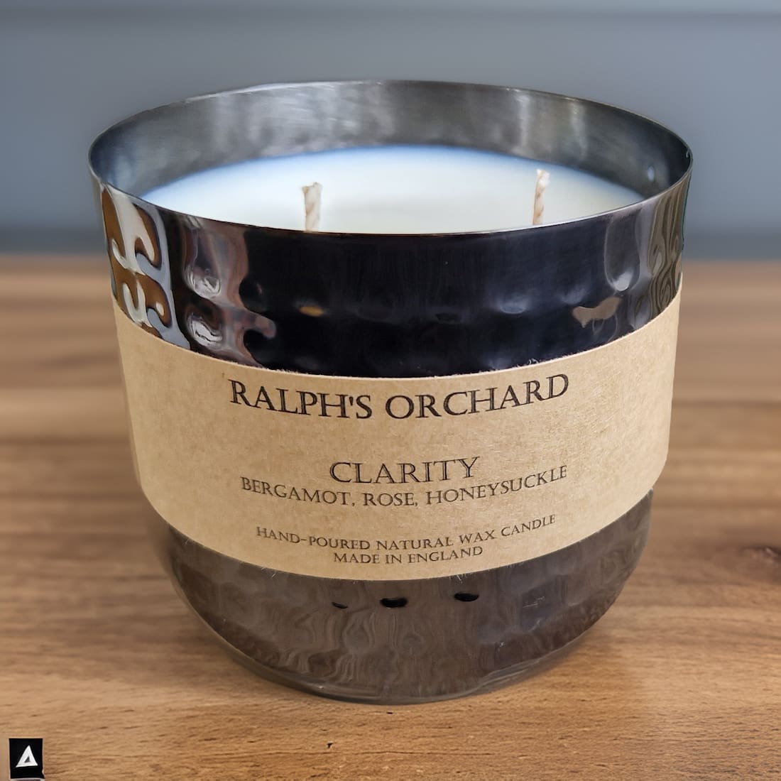 Candle labeled 'Ralph's Orchard Clarity' on a wooden surface with a neutral background