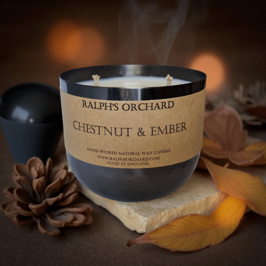 Candle labeled 'Ralph's Orchard Chestnut & Ember' with decorative elements on a dark background
