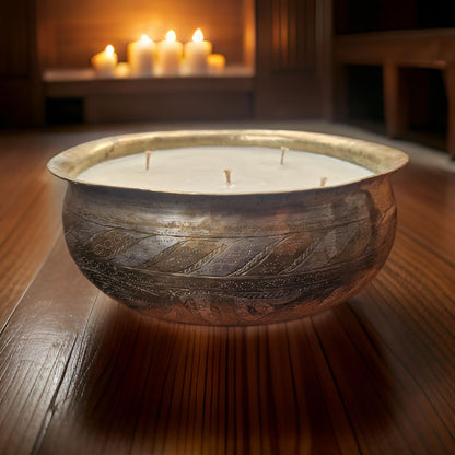 Decorative candle in a textured bowl on a wooden surface with candles in the background.