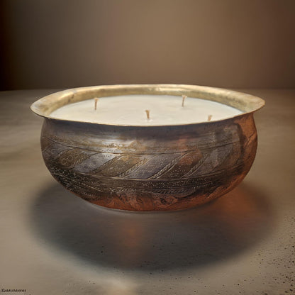 Decorative candle in a rustic metal bowl on a neutral background