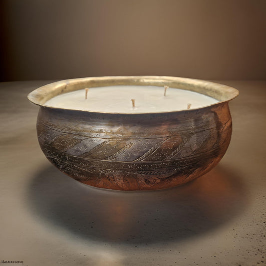 Decorative candle in a rustic metal bowl on a neutral background