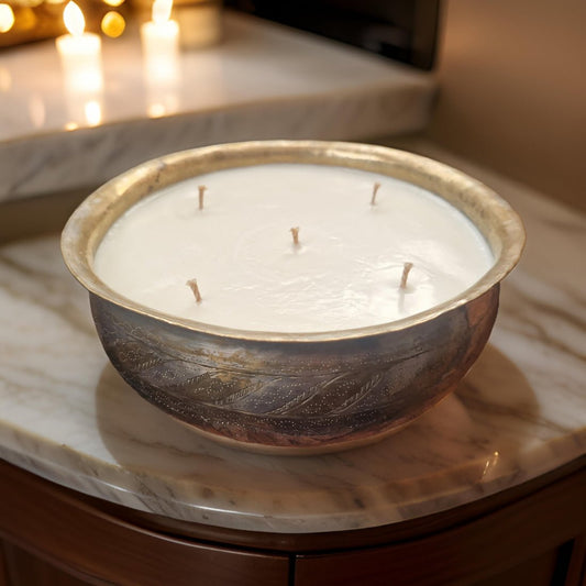 Decorative candle in a bowl on a marble surface with blurred lights in the background