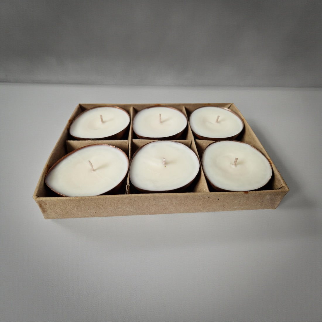 Set of six white candles in a cardboard box on a gray background