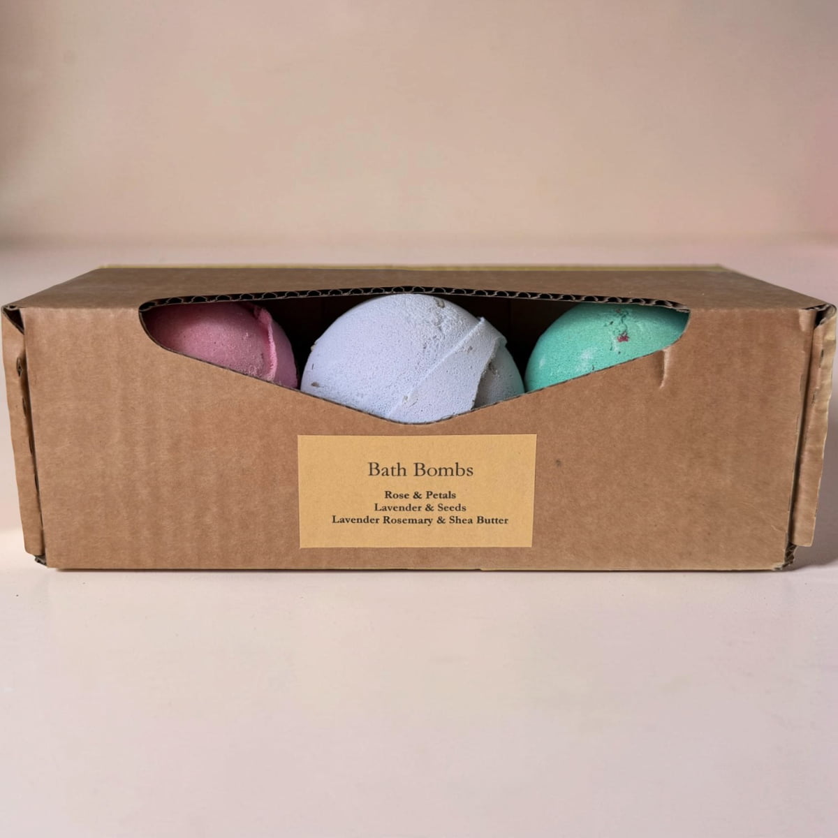 Three bath bombs in a cardboard box with a label on a beige background