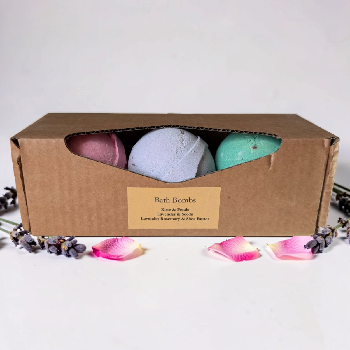 Three bath bombs in a cardboard box with a label, surrounded by decorative petals on a light background.