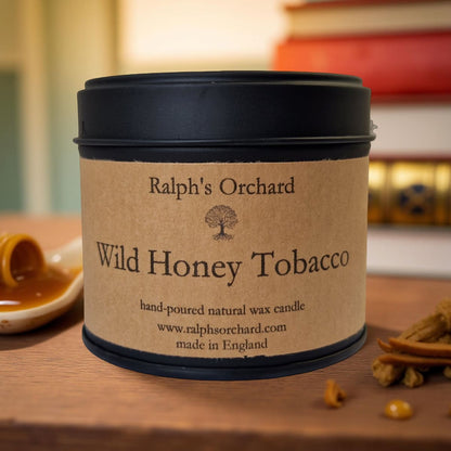Candle in a tin labeled 'Wild Honey Tobacco' by Ralph's Orchard on a wooden surface.