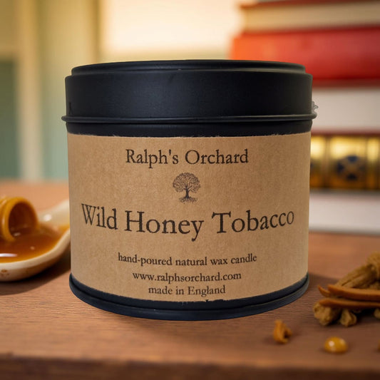 Candle in a tin labeled 'Wild Honey Tobacco' by Ralph's Orchard on a wooden surface.
