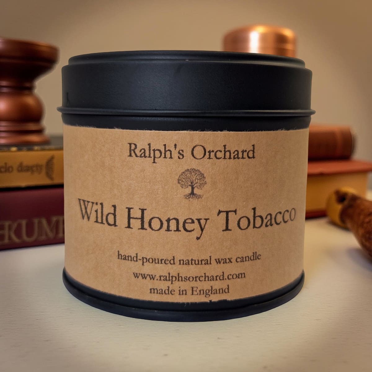Candle in a tin labeled 'Wild Honey Tobacco' by Ralph's Orchard on a wooden surface.