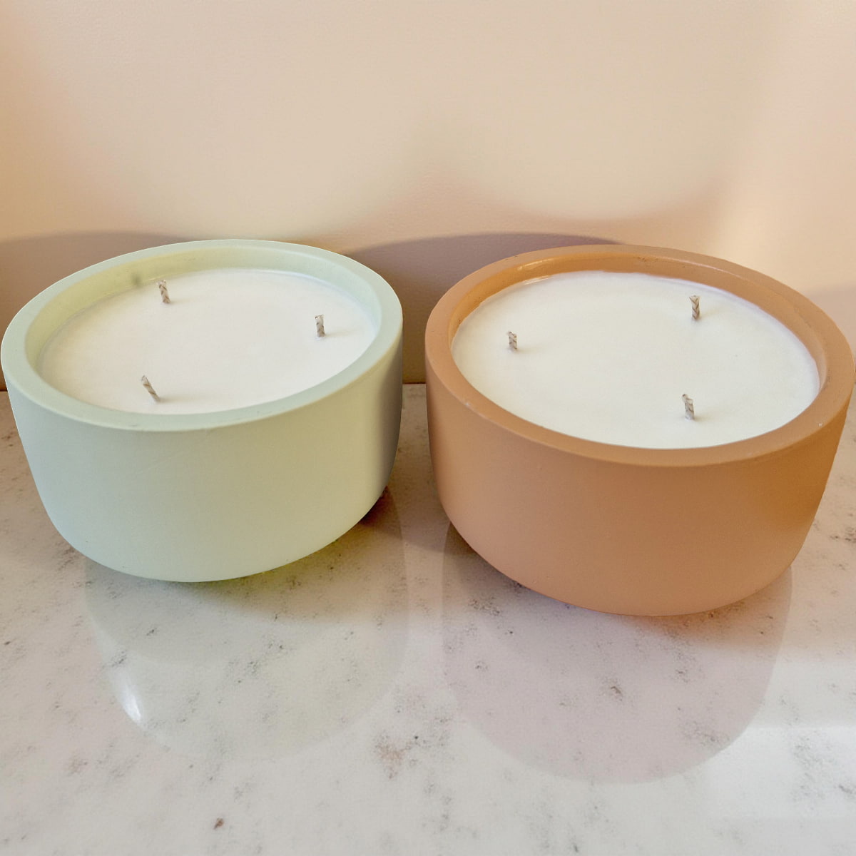 Two candles in terracotta pots on a marble surface with a soft pink background
