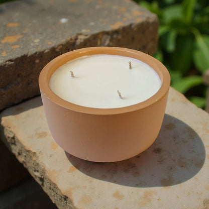 Candle in a terracotta pot on a stone surface with greenery in the background