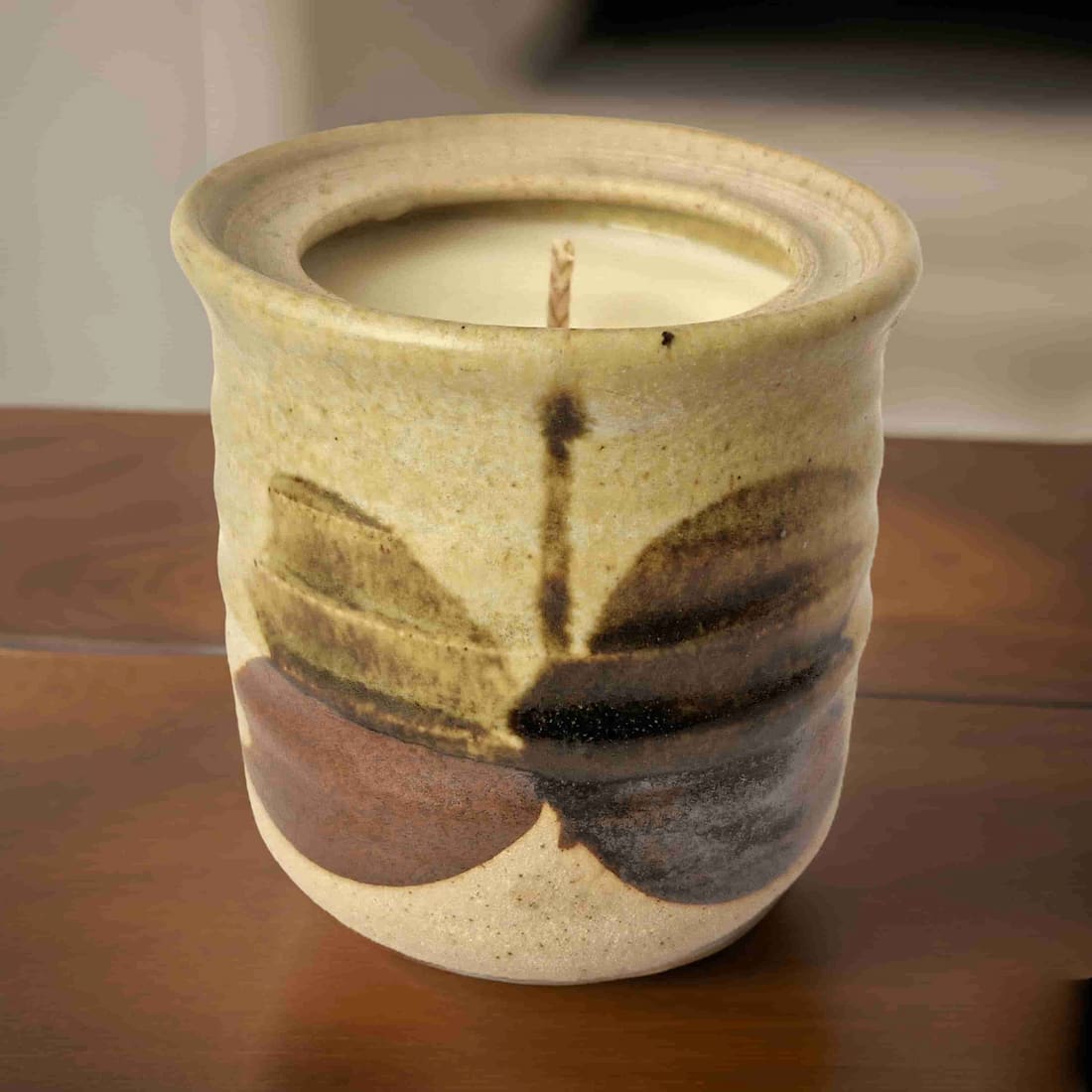 Ceramic candle holder with a lit candle inside on a wooden surface.
