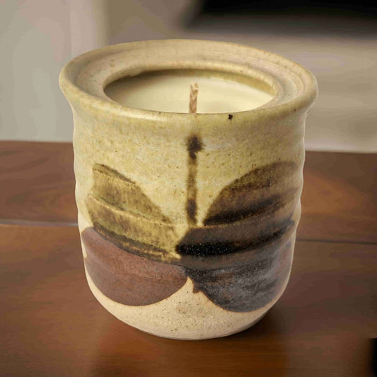 Ceramic candle holder with a lit candle inside on a wooden surface.