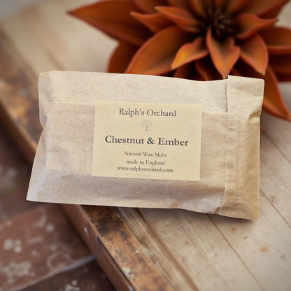 Wax melt package labeled 'Ralph's Orchard Chestnut & Ember' on a wooden surface with a plant in the background.