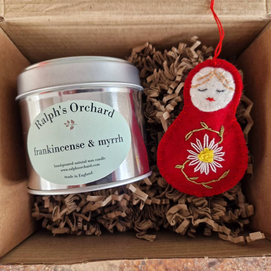 Candle labeled 'Ralph's Orchard' with a decorative red matryoshka doll in a box.