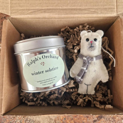 Candle labeled 'Ralph's Orchard winter solstice' and a small teddy bear with a bow in a cardboard box.