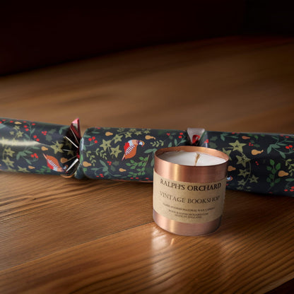 Candle with 'Ralph's Orchard Vintage Bookshop' label next to a decorative cracker on a wooden surface