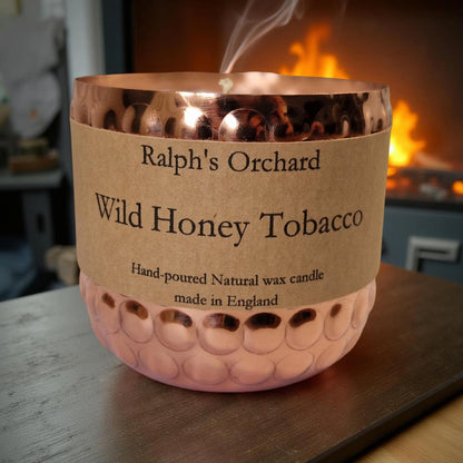 Candle labeled 'Ralph's Orchard Wild Honey Tobacco' with a fireplace in the background
