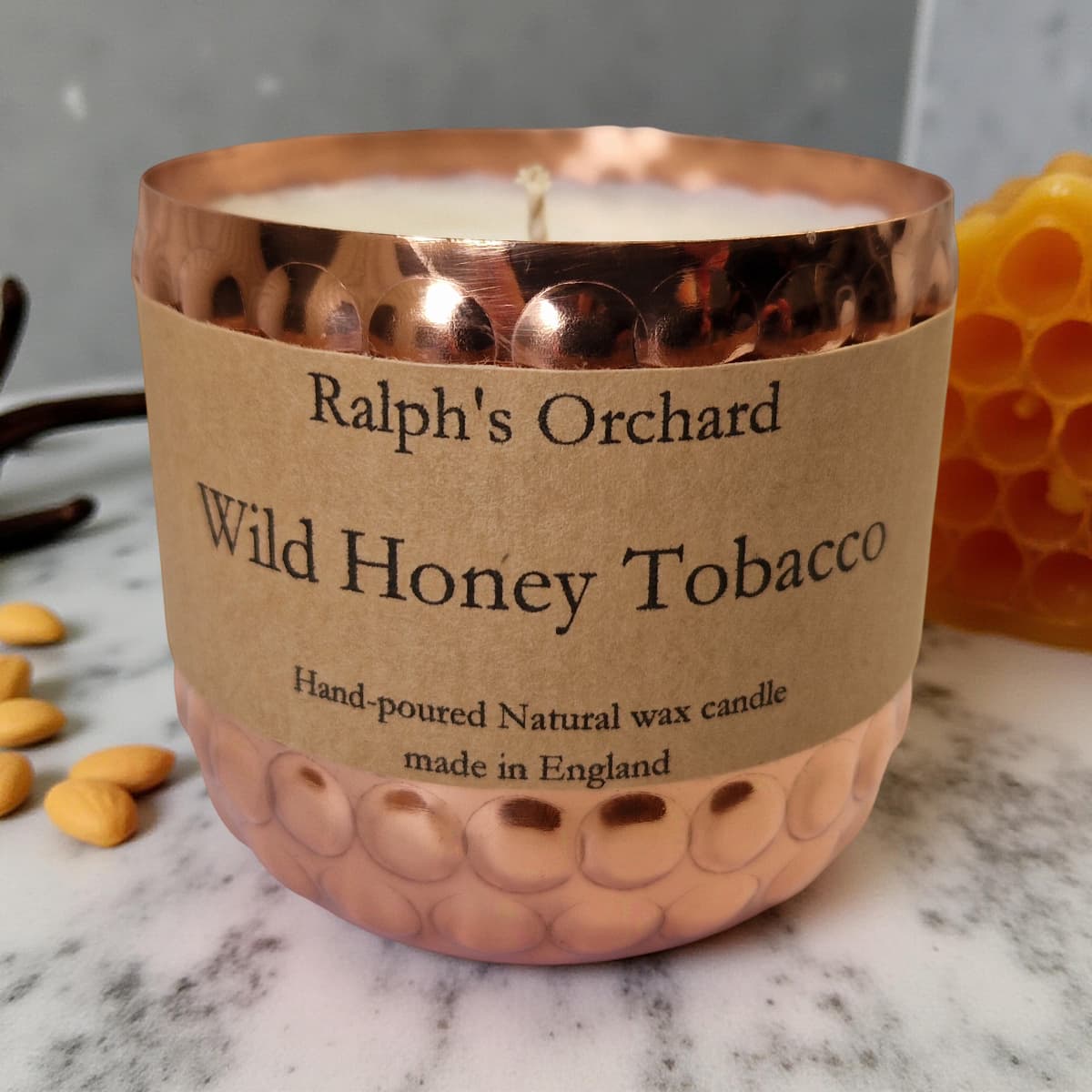 Candle labeled 'Ralph's Orchard Wild Honey Tobacco' with a copper lid on a marble surface.