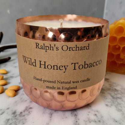 Candle labeled 'Ralph's Orchard Wild Honey Tobacco' with a copper lid on a marble surface.