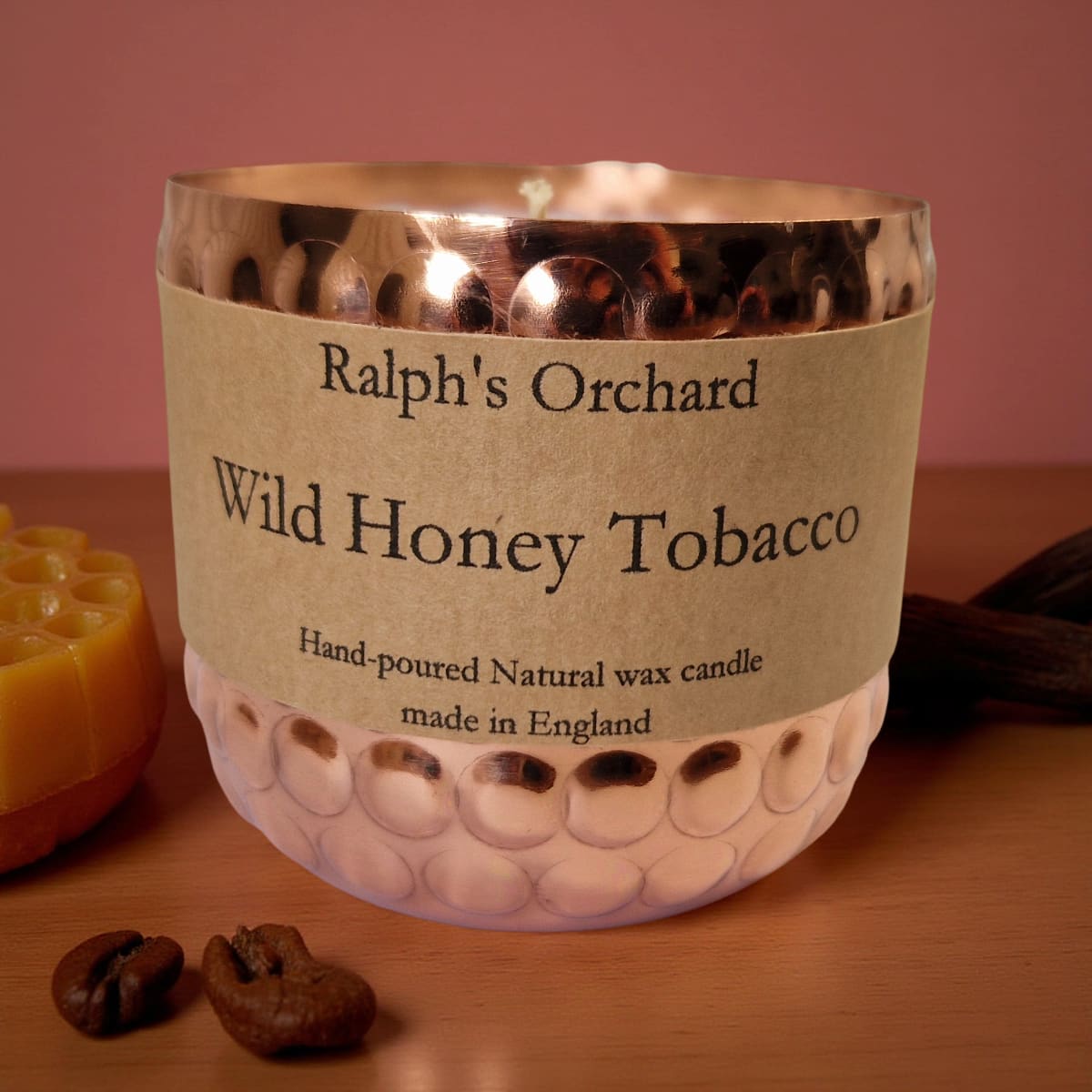 Candle labeled 'Ralph's Orchard Wild Honey Tobacco' on a wooden surface with coffee beans.