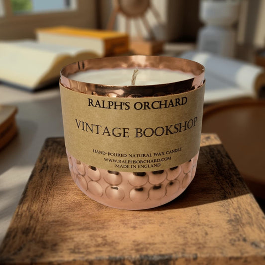Candle in a decorative holder labeled 'Ralph's Orchard Vintage Bookshop' on a wooden surface.