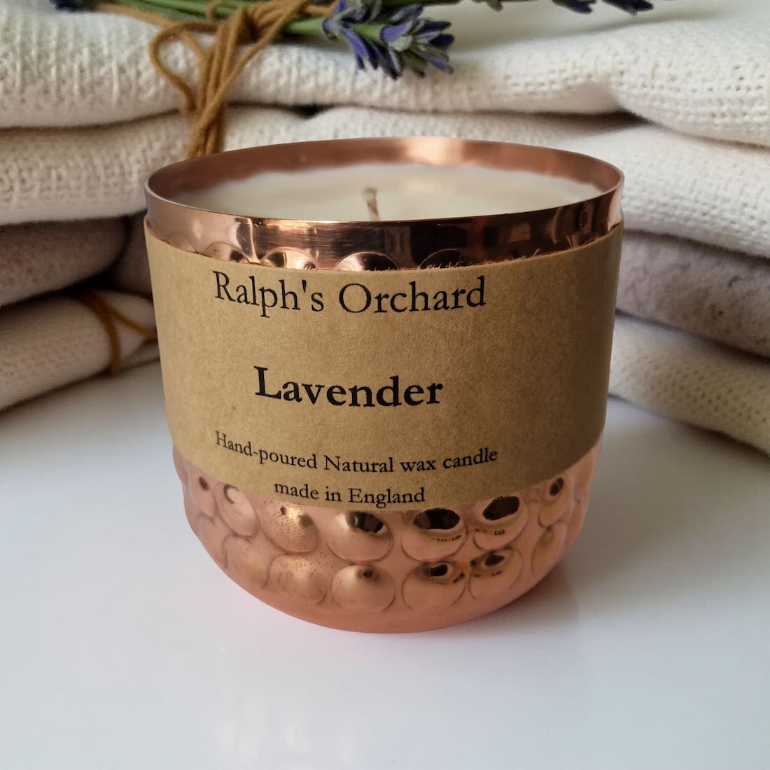 Candle in a copper container with 'Ralph's Orchard' label on a white surface