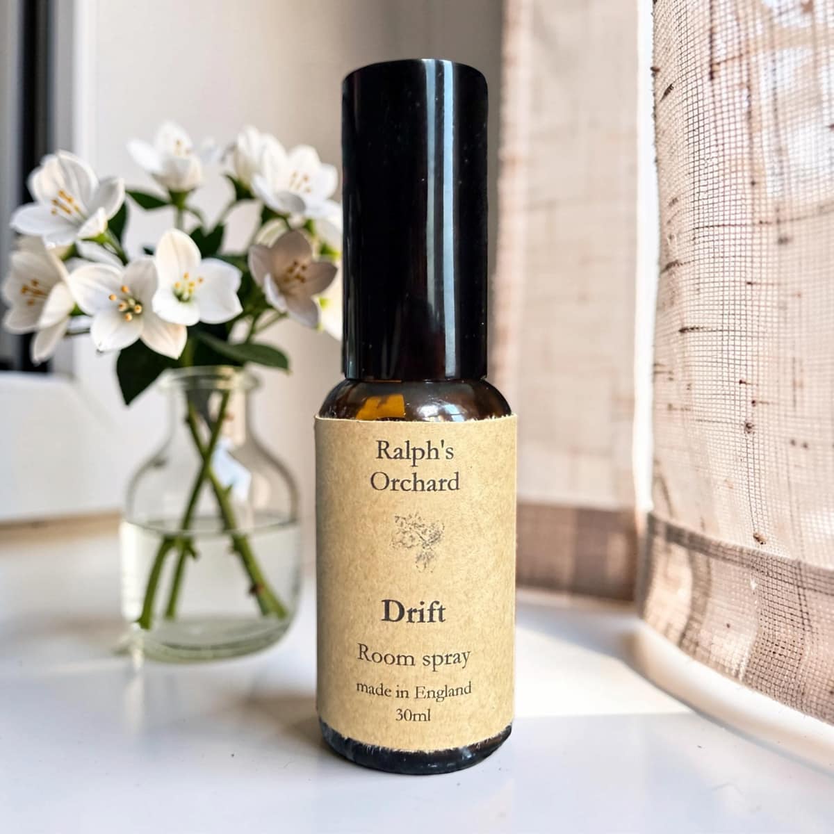 Bottle of Ralph's Orchard Drift room spray on a surface with flowers in the background