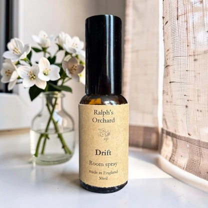 Bottle of Ralph's Orchard Drift room spray on a surface with flowers in the background