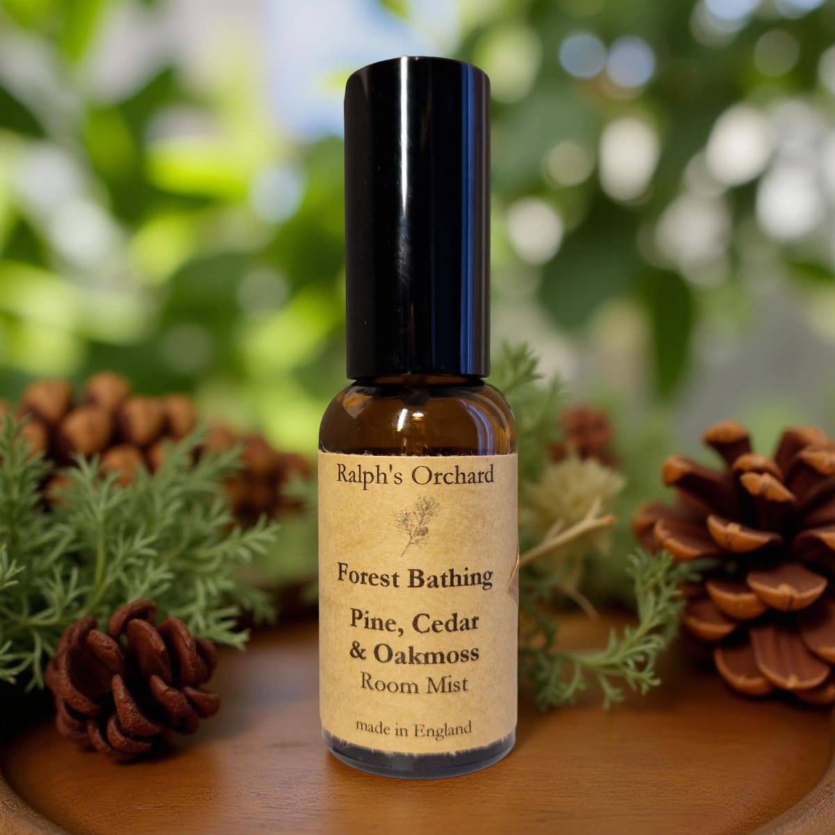 Bottle of 'Forest Bathing' room mist with pine cones and greenery on a wooden surface
