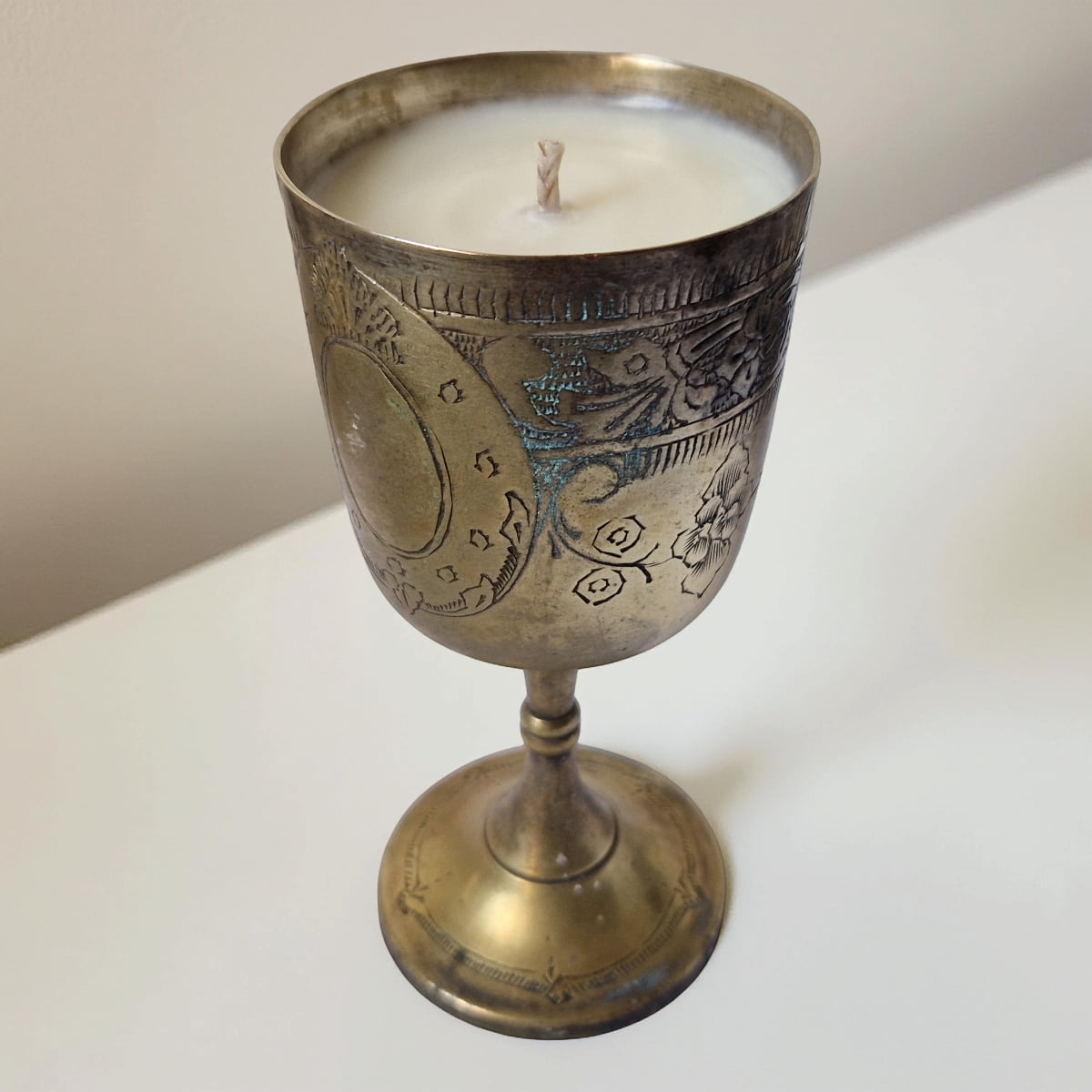 Decorative candle in an ornate brass holder on a white surface