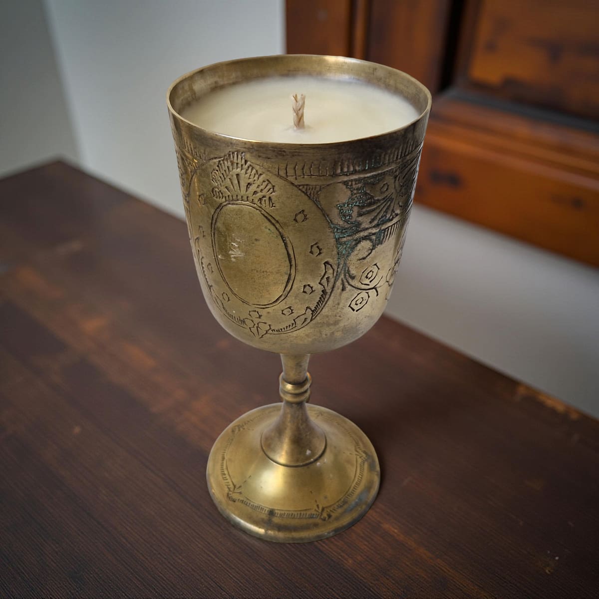 Decorative candle in a brass chalice on a wooden surface