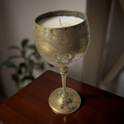Decorative candle in a brass wine glass on a wooden surface with a blurred background