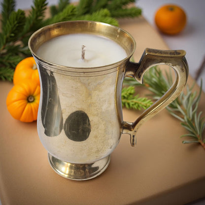 Silver mug with a candle inside, surrounded by pumpkins and greenery on a wooden surface.