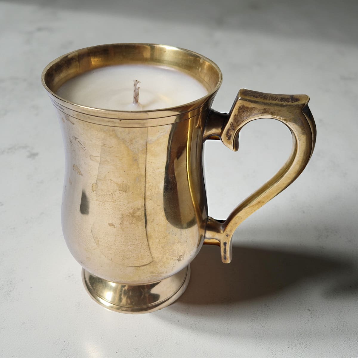 Brass mug with a candle inside on a light gray background
