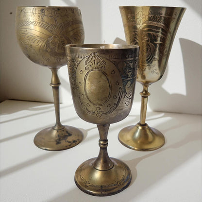 Three ornate brass goblets on a white surface with a neutral background